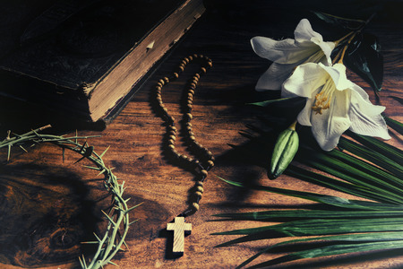 The Triumph, Passion, Crucifixion and Resurrection. Iconic Christian symbols representing events from Palm Sunday to Easter rest upon a rustic table along with a 19th century antique bible - palm branch, crown of thorns, cross, and white lily.