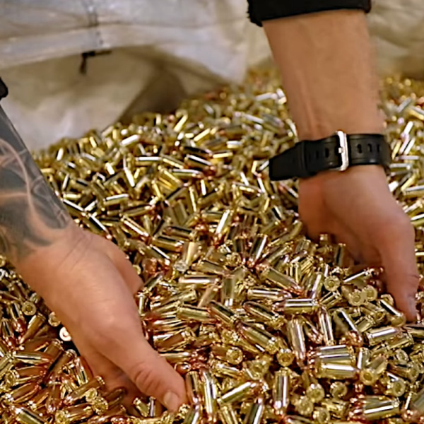 Two mens hands scooping up many bullets from a Remington factory bullet bin
